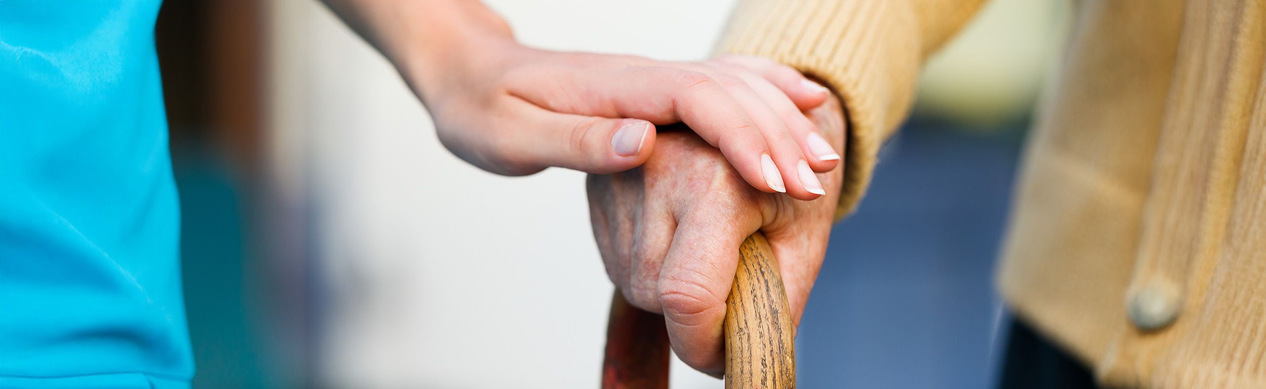 Pflegerin legt beruhigend ihre Hand auf die Hand einer Seniorin, die einen Gehstock hält